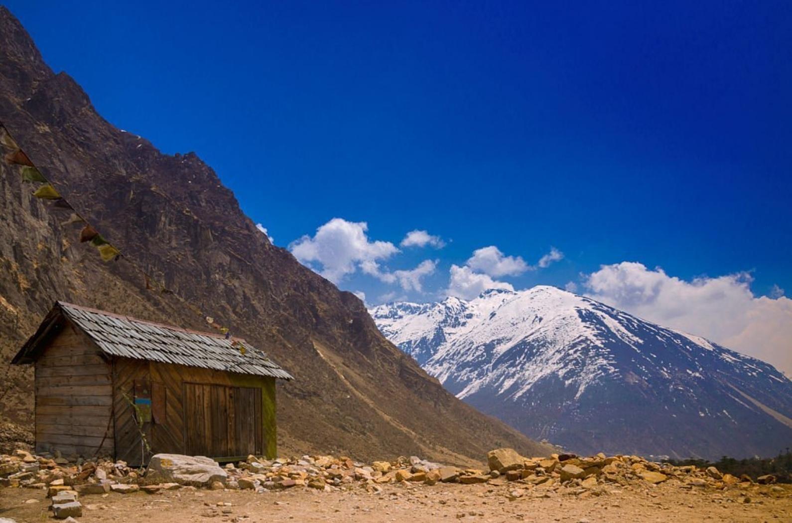 A wooden house with rock and snow mountain in background in Chopta Valley