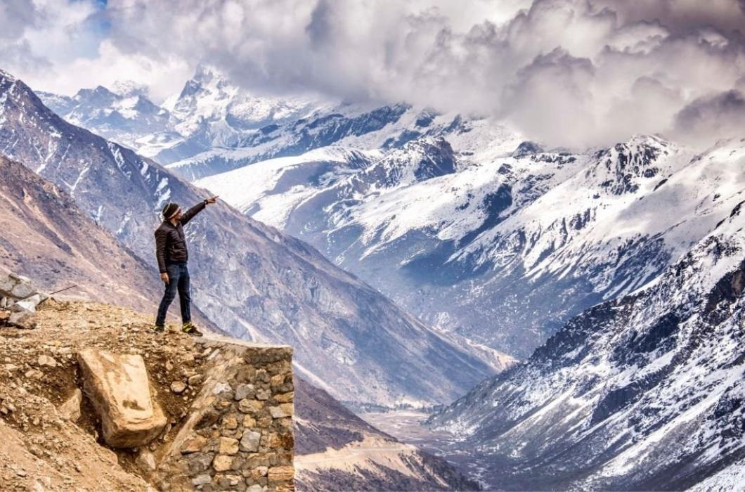 A young man on an adventure trip pointing finger at the mountain in Chopta Valley, North Sikkim, India