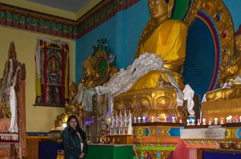 Girl standing near buddha golden statue at Bomdila monastery.