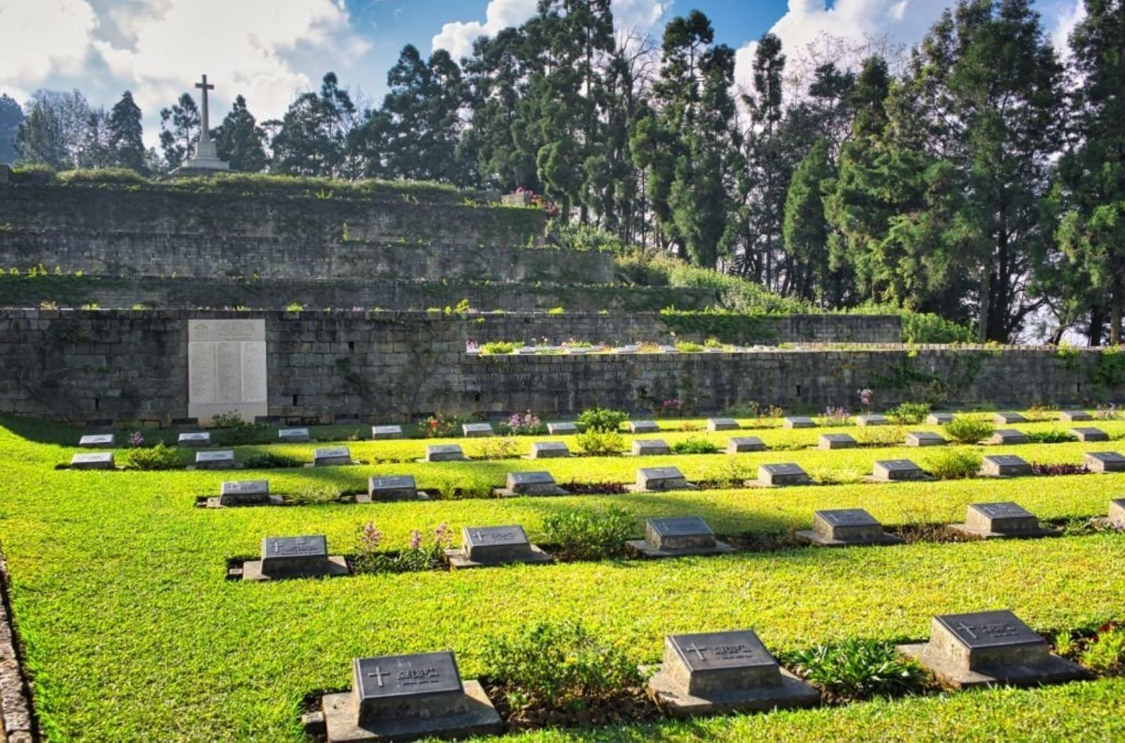 Beautiful sunlight flooding a white cross and all the grave stones in Kohima War Cemetery, surrounded by trees, during day time, Nagaland, INDIA