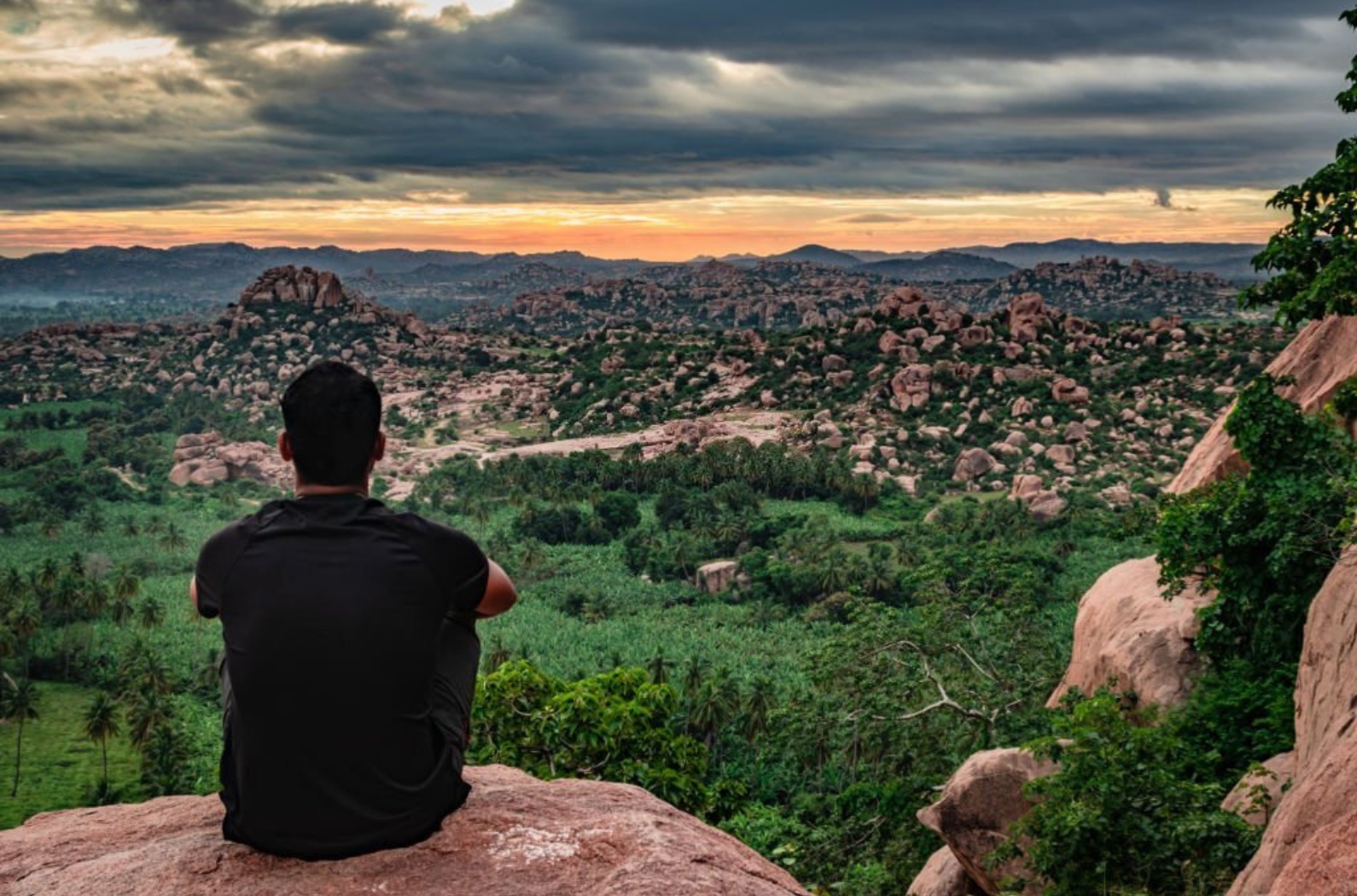 Man sitting at mountain top watching the sunrise with dramatic sky at morning flat angle shot is taken at Matanga hill.