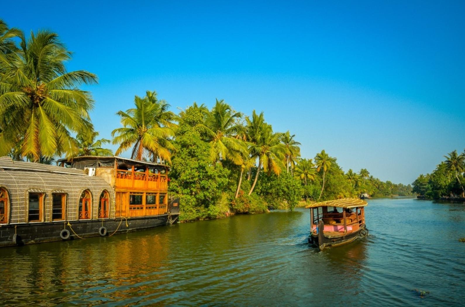 A tourist boat passes through a traditional Kerala houseboat on the backwater of Vembanad Lake.