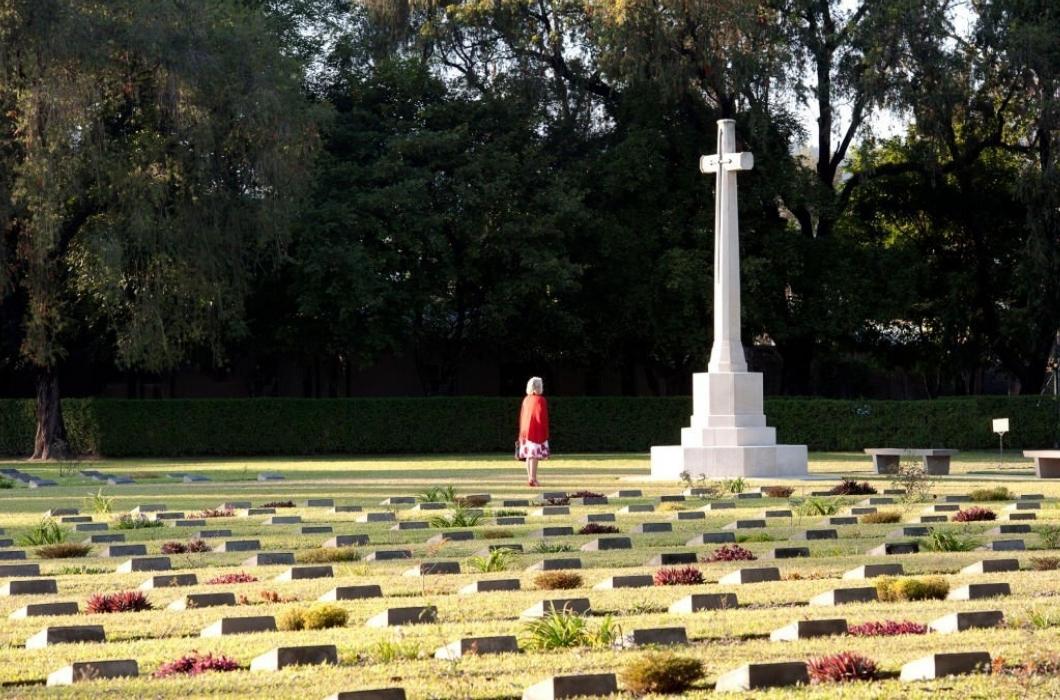 A visitor stands in quiet contemplation at Imphal War cemetery with its many carved and sculpted gravestones with etched lettering commemorating the dead British and Indian soldiers of WW2, Imphal, Manipur, India.