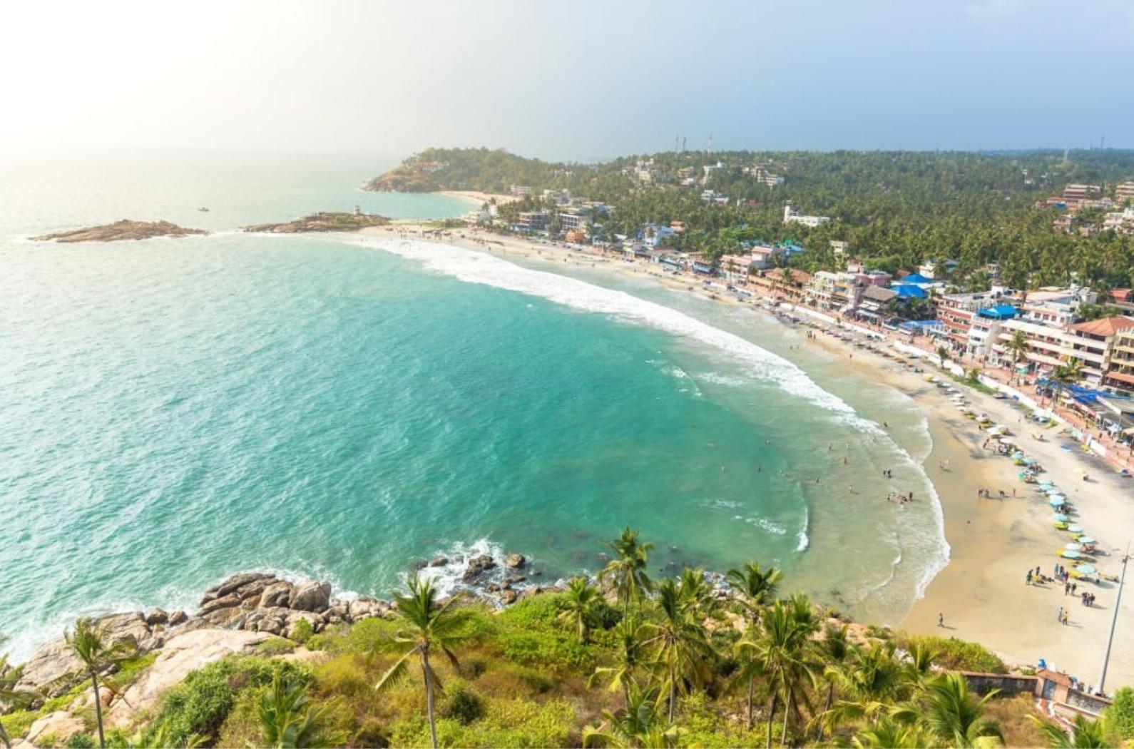 Aerial view of tourists taking a dip in the turquoise waters of Lighthouse beach at Kovalam, Trivandrum. Tropical feel with green coconut trees and blue waters.