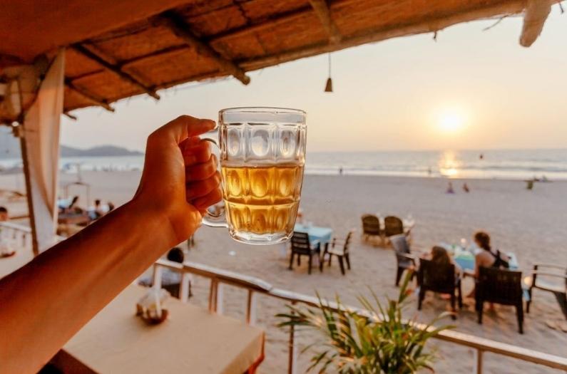 Beer mug in hand of tourist relaxing on a beach with lounge.