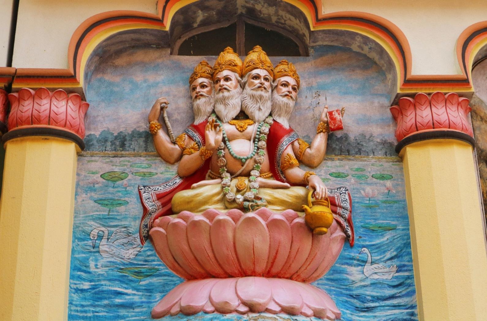 View of wall art of Hindu god Brahma. Brahma, the four-headed lord, sits on a lotus flower. Religious image on the temple in India.