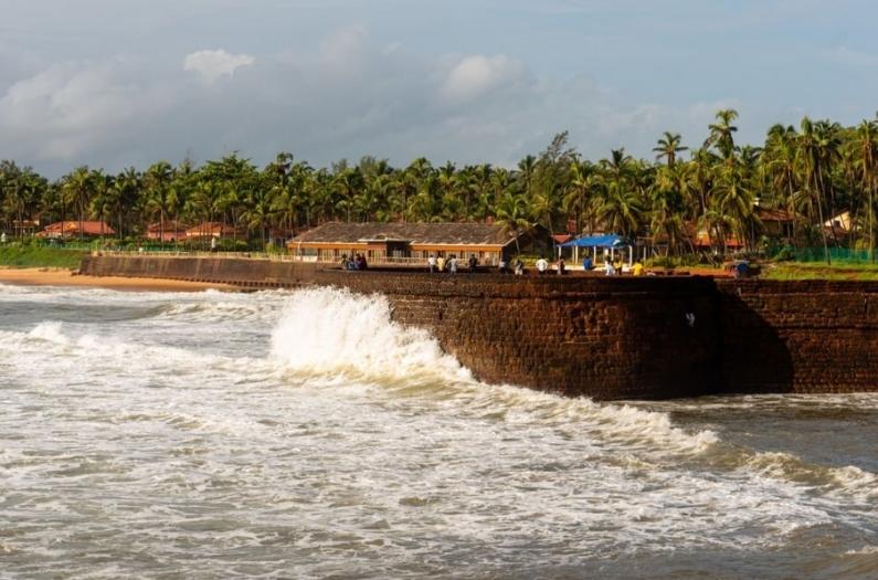 Waves crashing on the Sinquerim fort with the beach landscape in the background in Goa.