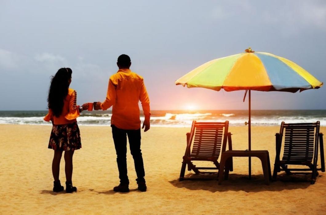 Young couple standing near deck chair and umbrella on tropical sandy Calangute beach .