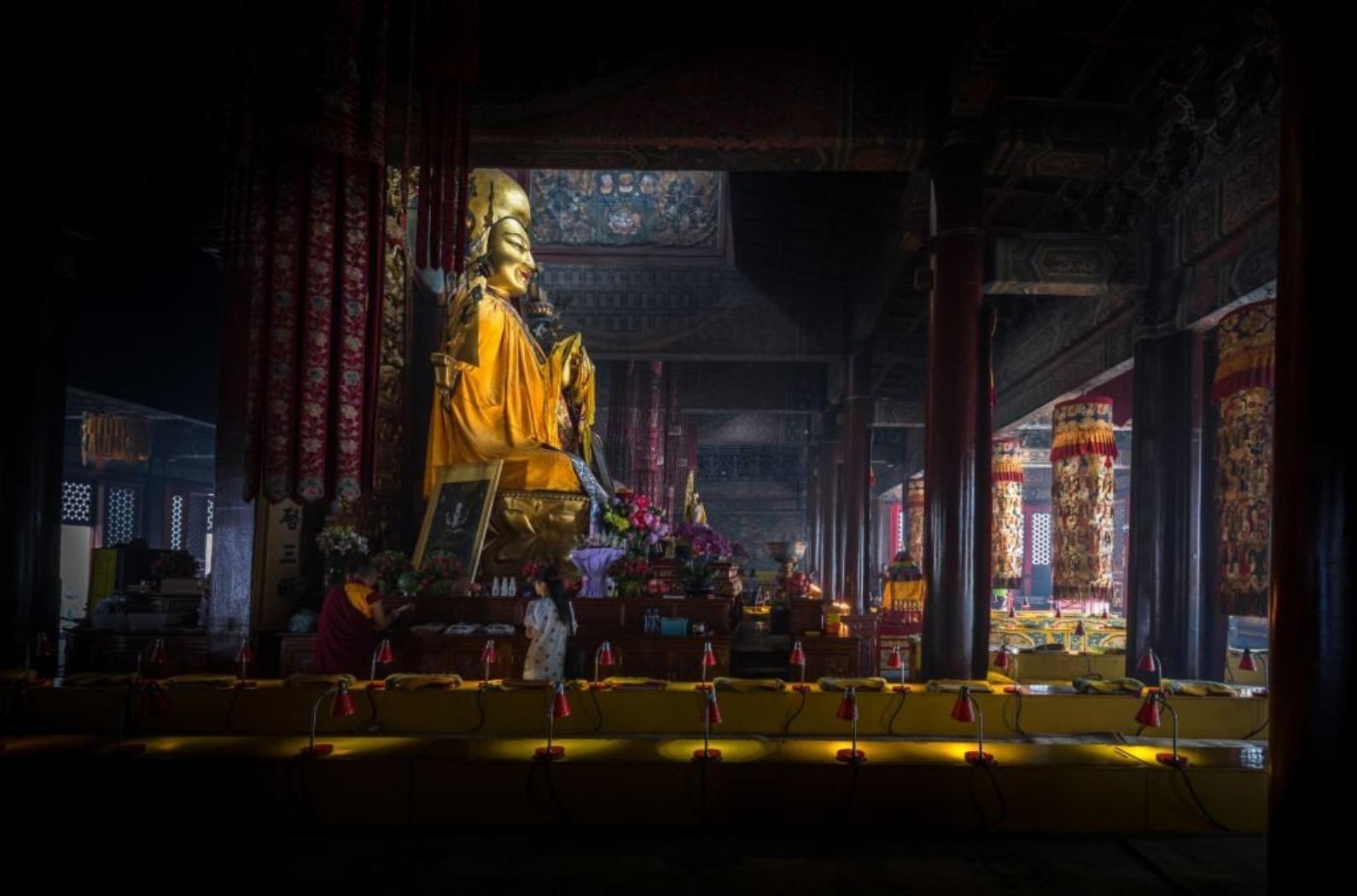 The image shows the inside of the famous Lama temple in Beijing with a huge golden buddha.