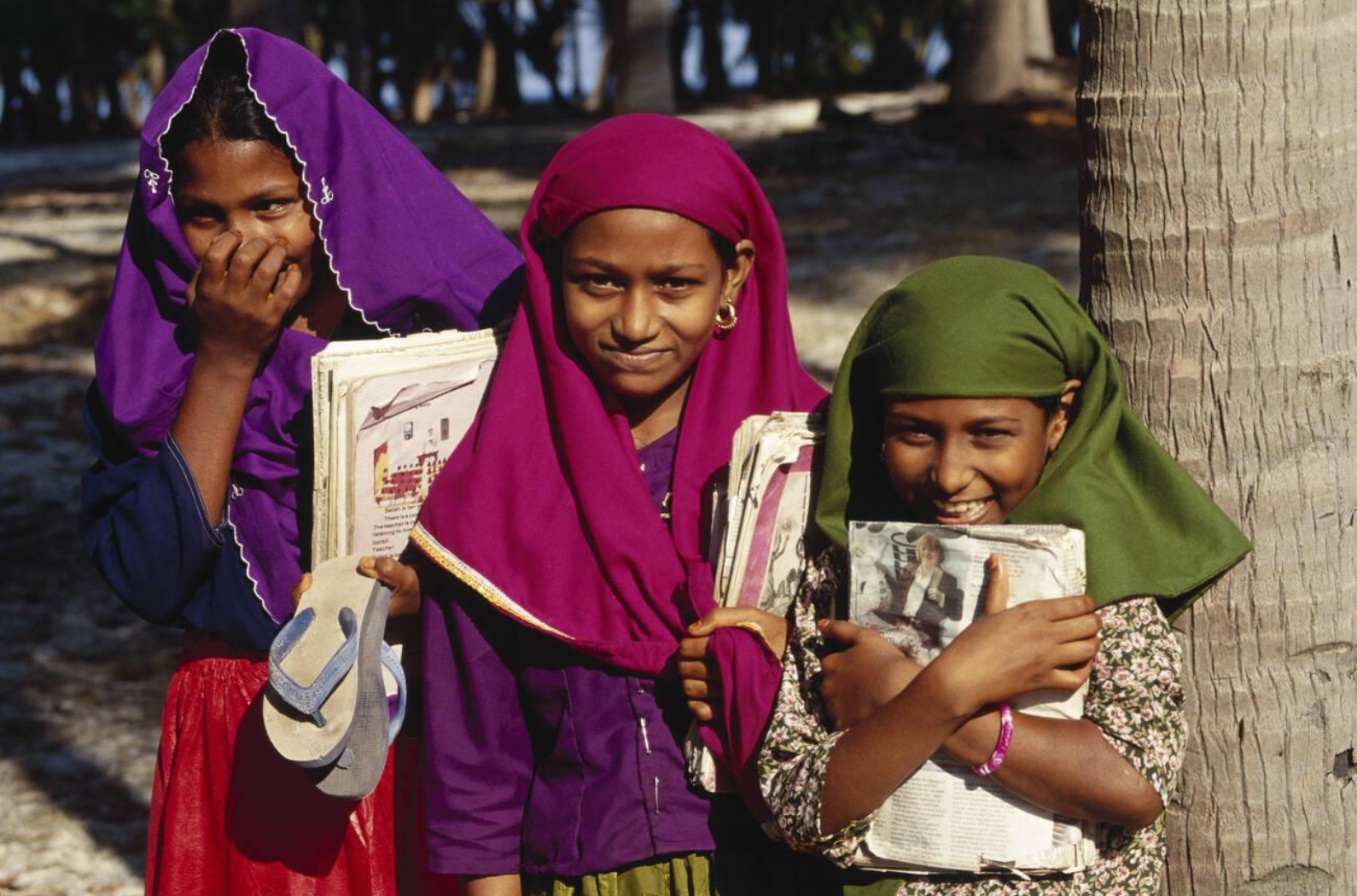 Muslim three girl students shy smiling laugh books in hand head covered going to school