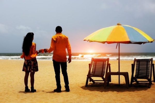 Young couple standing near deck chair and umbrella on tropical sandy Calangute beach .